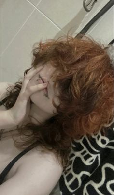 a woman with red hair is laying on the floor in front of a mirror and holding her hand to her face