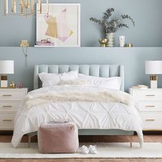 a bedroom with blue walls, white bedding and gold accessories on the nightstands