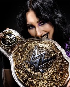 a woman holding up a gold and silver wrestling belt with an embellishment on her face