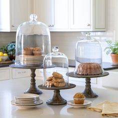 three tiered trays with cakes and pastries under glass covers on a kitchen counter