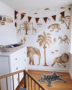 a baby's room with animals and trees on the wall next to a crib