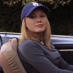 a woman sitting in the back seat of a car wearing a blue hat and gray shirt