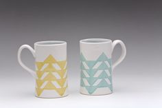 two coffee mugs sitting side by side on a white surface with blue and yellow designs