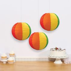 three paper lanterns hanging from the ceiling above a table with cake and cupcakes