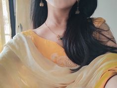 a woman with long black hair wearing a yellow sari and gold jewelry, looking out the window