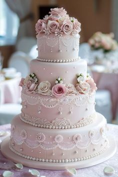 a three tiered wedding cake with pink flowers and pearls on the top is sitting on a table