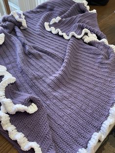 a purple blanket with white ruffles sitting on top of a wooden table