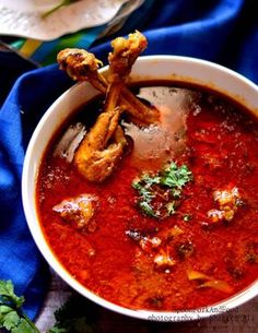 a white bowl filled with red sauce and chicken wings on top of it next to some parsley