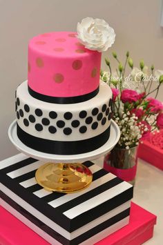 a three tiered cake with polka dots and pink, black, and white designs