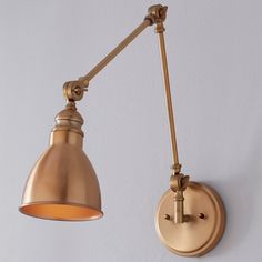 an old fashioned wall light with a metal arm and gold shade on the side, against a white background