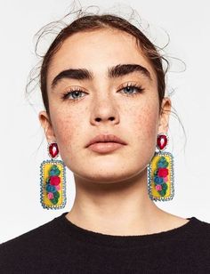 a woman with freckles on her face is wearing earrings that are decorated with flowers