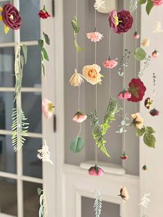 an arrangement of paper flowers hanging from the ceiling in front of a white door and window