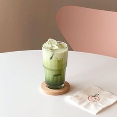 a drink sitting on top of a white table next to a napkin with a green liquid in it