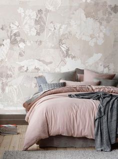 a bed with pink comforter and pillows in front of a floral wallpaper