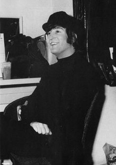 a black and white photo of a man in a hat sitting on a chair smiling