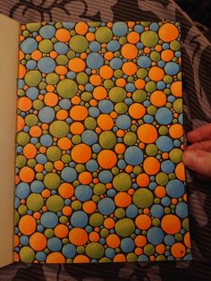 an open book with orange and blue balls on it, sitting on a patterned surface