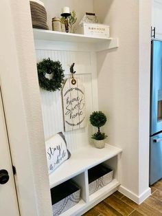 a white shelf filled with plants and other items on top of a wooden floor next to a refrigerator