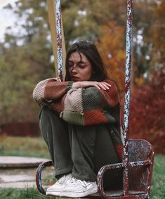 a woman sitting on a swing with her head resting on her hands and arms crossed