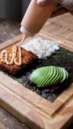 the person is cutting up some food on the wooden board with chopsticks and an avocado