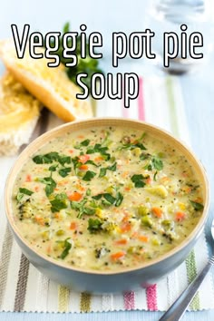 a bowl of vegetable pot pie soup on a table with bread and spoons next to it