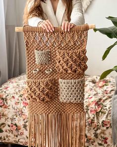 a woman is holding up a woven wall hanging with fringes and beadwork