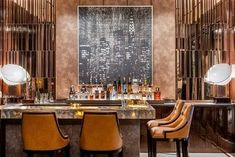 a bar with two chairs and bottles on the counter in front of an art work