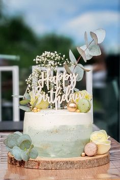 a birthday cake sitting on top of a wooden table next to flowers and greenery