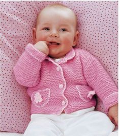 a baby laying on top of a bed wearing a pink sweater and white pants with polka dots