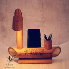 a cell phone and pen holder made out of wood with arabic writing on it,