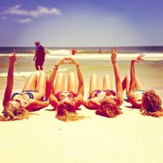 four women laying on the beach with their hands in the air and one woman standing behind them