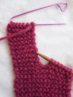 a pink knitted mitt next to a knitting needle