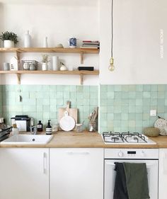 a kitchen with white cabinets and green tile backsplash, shelves above the stove