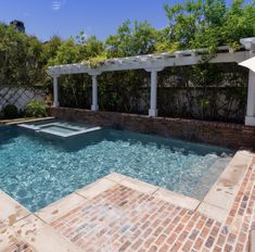 an outdoor swimming pool with brick pavers and pergolated patio area in the background