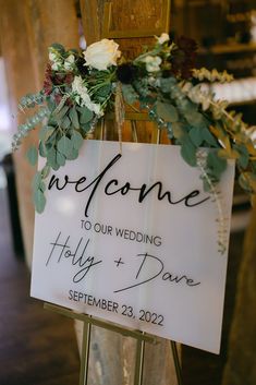 a welcome sign with flowers and greenery on it is attached to a wooden post