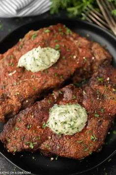 two pieces of meat on a black plate with white sauce and parsley sprinkled on top