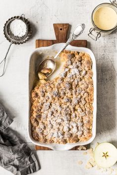 an apple cobbler with powdered sugar on top and two spoons next to it