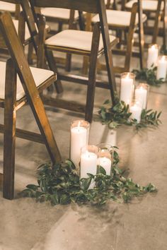 candles are lined up on the floor in front of rows of chairs with greenery