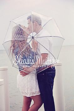 a man and woman kissing under an umbrella on a pier near the water with their arms around each other