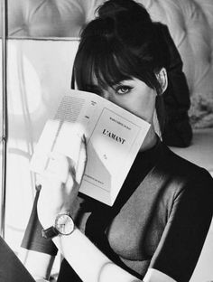 a black and white photo of a woman holding an empty book over her face while sitting on a couch