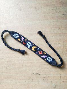 an old style bracelet with skulls and crossbones is on a wooden table next to a black cord