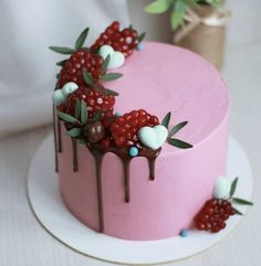 a pink cake decorated with berries and chocolate drips