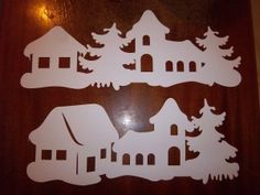 three cutouts of houses and trees on a wooden surface with light shining in the background