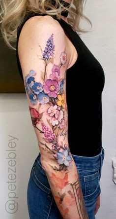 a woman with a flower tattoo on her left arm and right arm is wearing blue jeans