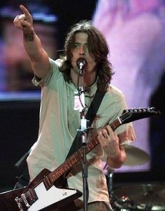 a man with long hair holding a guitar and pointing at something in front of him