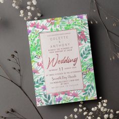 the wedding card is next to some flowers and branches on a gray surface with white blooms