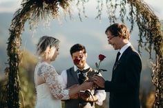 a bride and groom exchanging vows in front of an arch with greenery on it