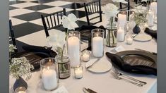 the table is set with black and white plates, silverware, candles and flowers