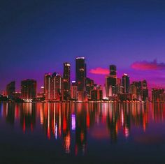 the city is lit up at night and reflecting in the water