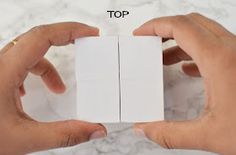 two hands holding small white cards on top of a marble surface with the word top written below it