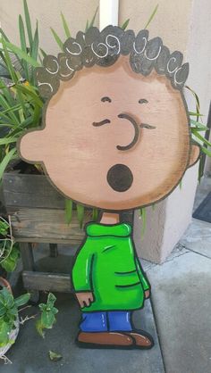 a wooden cutout of a cartoon character with grass in his mouth, standing next to a potted plant